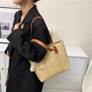 Detail of beige straw tote bag with brown leather straps and white lace decorative edging