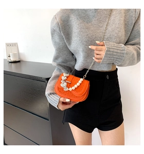 Detail van oranje mini-crossbodytas met parelketting en zilveren hartgespen op de flap