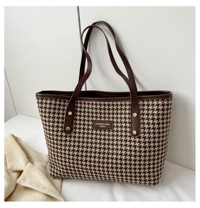 Close-up of vintage houndstooth tote bag with brown leather handles and gold rivet details