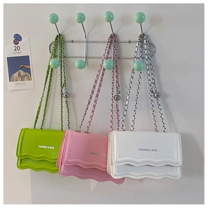 Detailed view of the wavy flap design and chain strap on three colorful square bags