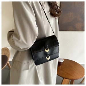 Detail view of a black leather crossbody bag with gold chain strap and metal buckles