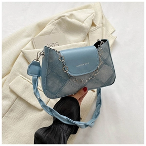 Détail du sac à bandoulière bleu clair texture denim avec chaîne fleurie et bandoulière corde
