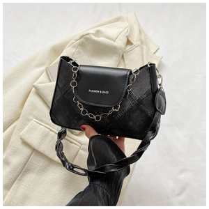 Gros plan d'un sac bandoulière noir avec chaîne argentée, boucle fleur et poignée tressée