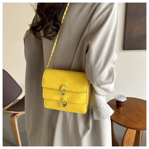 Detailed view of yellow leather shoulder bag with gold chain strap on a wooden table