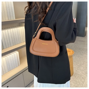 Brown leather half-moon crossbody bag with gold hardware and top handle on a model