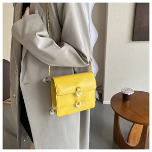 Detail of yellow shoulder bag featuring dual gold horseshoe buckles and leather texture