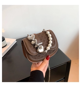 Detail van bruine mini zadeltas met parelketting handvat en zilveren hartjes