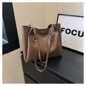 Detail of dark brown leather tote with golden metal chain strap on minimalist background