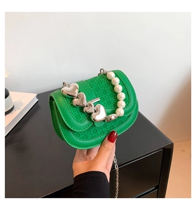 Detail van groene tas met steenpatroon, hartvormige sluiting en parelhandvat