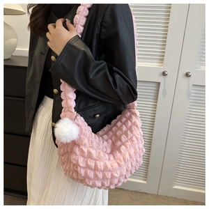 Detail of pink pleated crossbody bag featuring a soft bubble texture and plush pompom charm