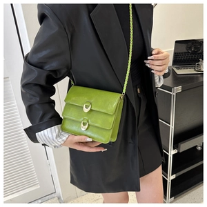 Detail of green vintage patent leather handbag with dual gold half-ring buckles and chain strap