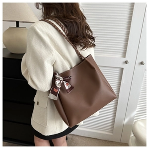 Detail of a large brown leather tote bag featuring a woven strap and patterned silk scarf
