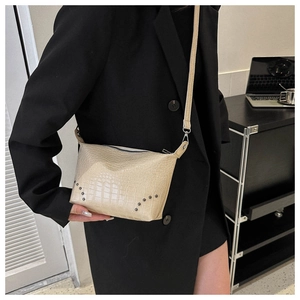 Detailansicht der cremefarbenen Krokoprägung-Tasche mit Nieten auf einem Business-Blazer