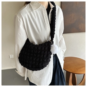 Detail of black popcorn texture shoulder bag with white plush ball charm on a model