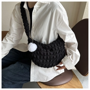 Detail of black pleated texture shoulder bag with white faux fur pompom charm on a model