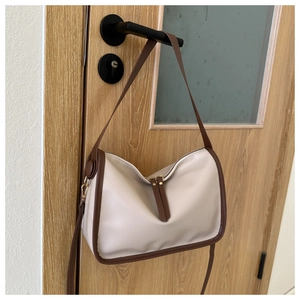 Detail of cream and brown faux leather tote bag hanging on a modern door handle