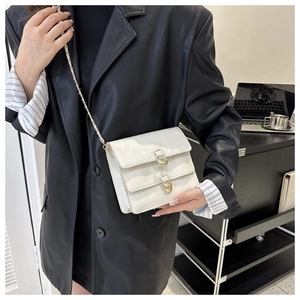 Detail of white leather crossbody bag featuring dual flap design and gold metal buckles