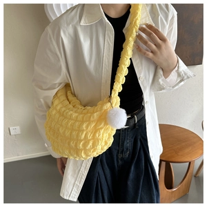 Detail of yellow pleated bubble crossbody bag with plush ball charm shown on a model