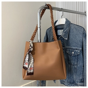 Detail of a large brown tote bag with woven handles and a decorative geometric silk scarf