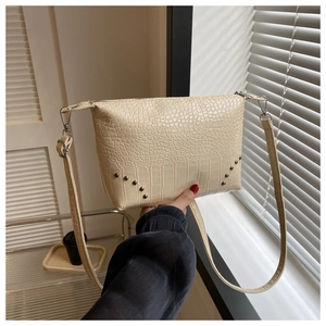 Detail der beigen Krokodilmuster-Textur und Silbernieten auf einer Lederhandtasche