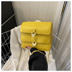 Detail of bright yellow leather handbag with gold oval buckles and woven chain strap