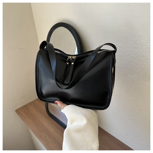 Close-up of minimalist black leather tote bag featuring sleek dual metal zippers and strap