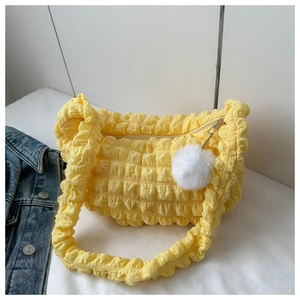 Detail of yellow pleated bubble shoulder bag featuring a soft white plush pom-pom charm