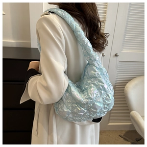 Side view of a light blue iridescent quilted puff bag worn by a model in a modern room