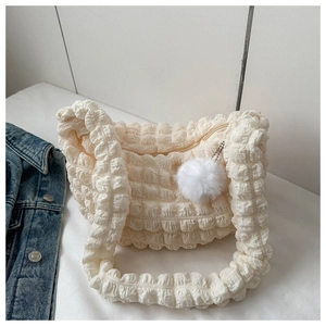 Detailed view of cream bubble fabric texture and white fur ball charm on shoulder bag