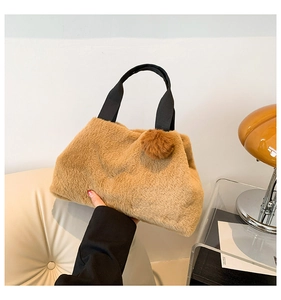 Detail einer weichen braunen Plüschtasche mit schwarzem Griff und dekorativem Fellbommel
