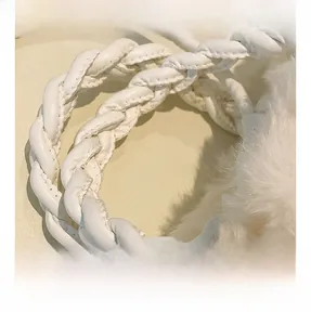 Macro shot of woven leather handle and fluffy white faux fur texture on a cream crossbody bag