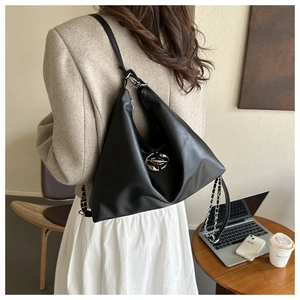 Detail of black triangular PU leather bag with metal emblem on a beige coat outfit