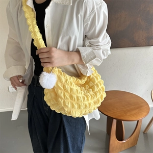 Fashionable yellow pleated shoulder bag with bubble texture and white plush charm on a model