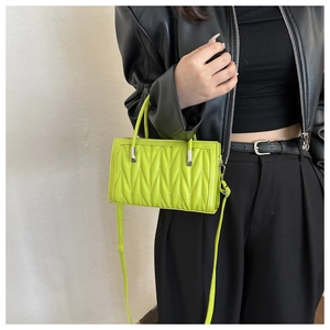 Detail of neon green quilted handbag with V-stitch texture held by model in black outfit