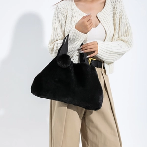 Schwarze Plüsch-Tragetasche mit W Studio Etikett, präsentiert von einem Model im Strickoutfit