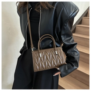 Brown pleated crossbody bag styled with a leather jacket on a minimalist staircase