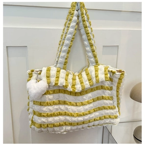 Détail de la texture gaufrée rayée jaune et blanc du sac cabas avec charme de cœur