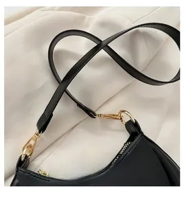 Close-up of black crossbody crescent bag with gold metal hardware and zipper detail