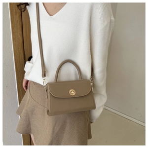 Detail showing khaki brown leather crossbody bag with golden clasp worn by a model