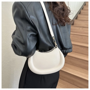 Creamy white crescent shoulder bag with gold hardware worn over a black leather jacket