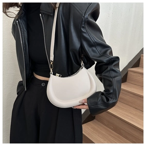 Detailed view of a white PU leather crescent bag with a slim strap worn with a black jacket