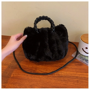 Detail of black faux fur cloud bag with woven handle and plush texture on wooden surface