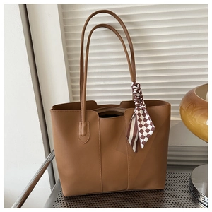 Detail of a large brown tote bag featuring slender shoulder straps and a checkerboard scarf