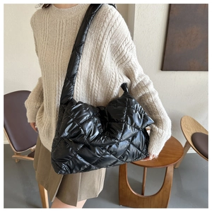 Close-up of black quilted puffer shoulder bag with puffy texture and wide strap on model