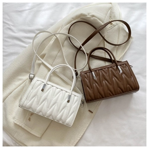 Detail of white and brown crossbody bags with quilted wave pattern on a beige blazer
