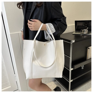 Detailed side view of white faux leather tote bag held by model in modern office setting