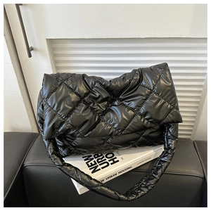 Close-up of black quilted puffer shoulder bag with elegant rhombic texture on a sofa