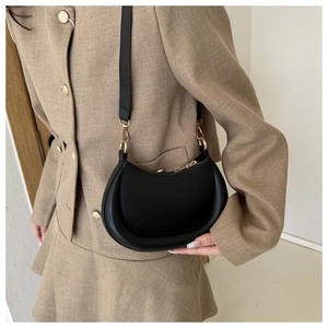 Close-up of minimalist black leather crescent bag with elegant gold hardware on a model