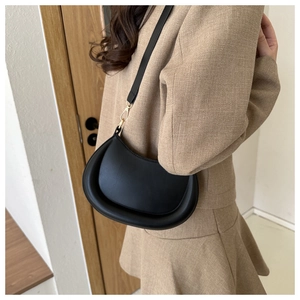 Detail of minimalist black crescent bag with golden hardware on a beige textured suit
