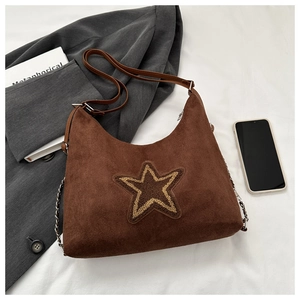 Détail du sac hobo en daim marron avec patch étoile sur fond de tissu blanc plissé